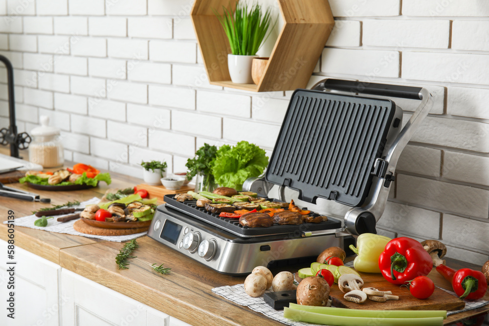 Modern electric grill with tasty vegetables on table in kitchen