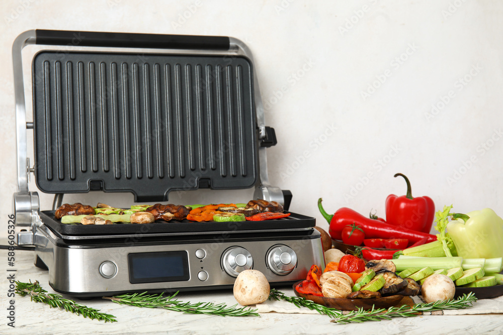 Modern electric grill with tasty vegetables on light background