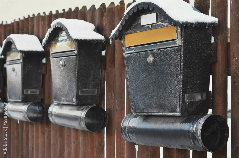 View of metal mailboxes with snow on wooden fence, closeup