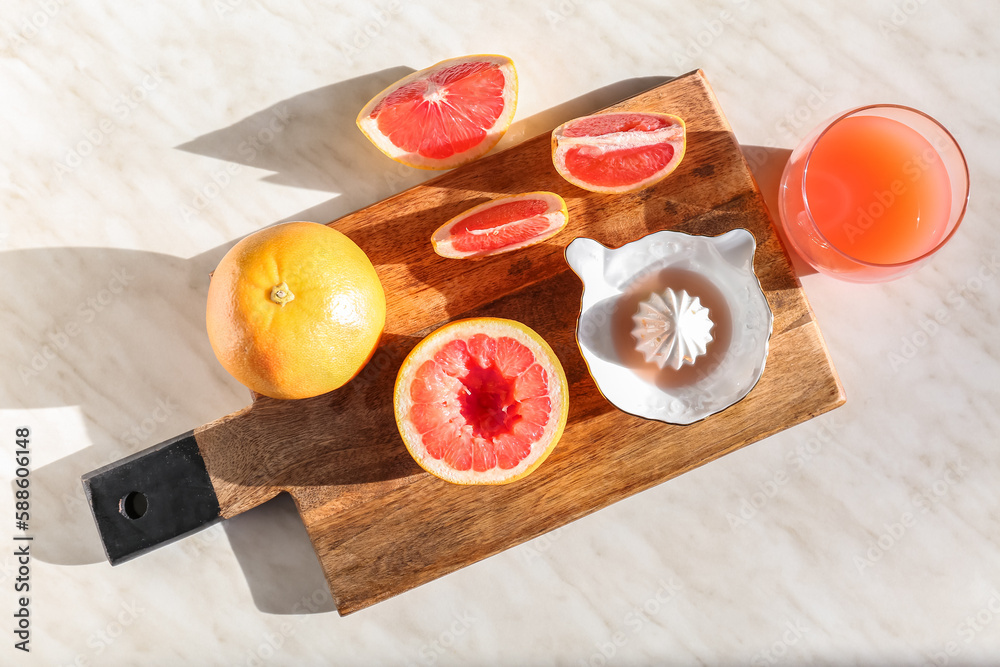 Wooden board with ripe grapefruits, glass of juice and juicer on light background