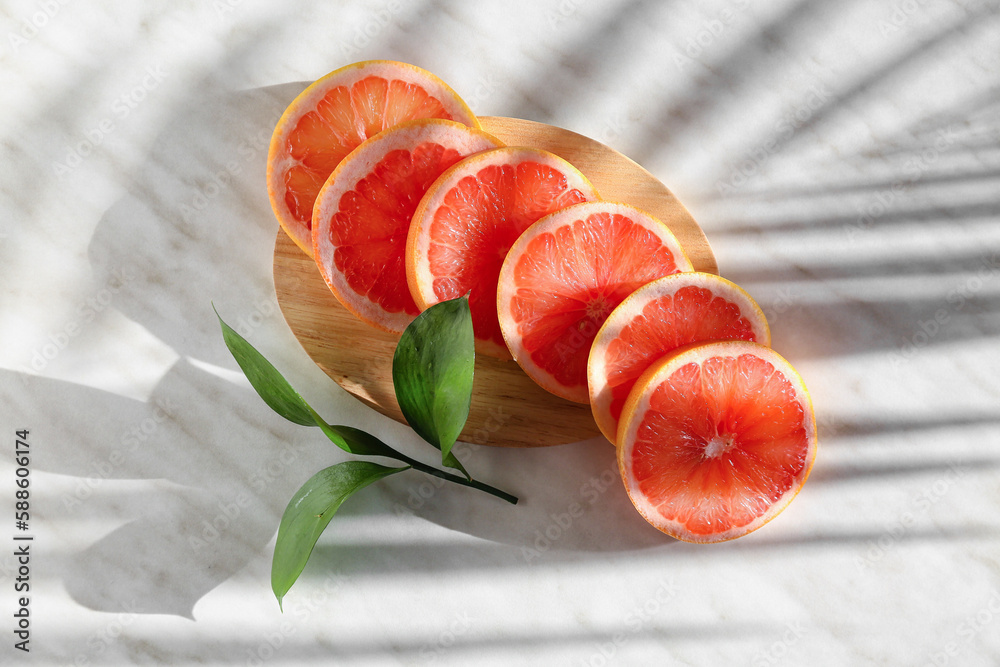 Wooden board with slices of ripe grapefruit and plant branch on light background