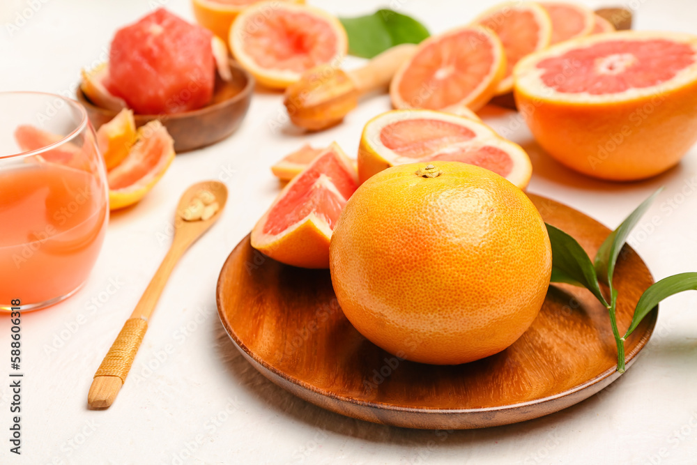 Wooden plate with ripe grapefruits on light background