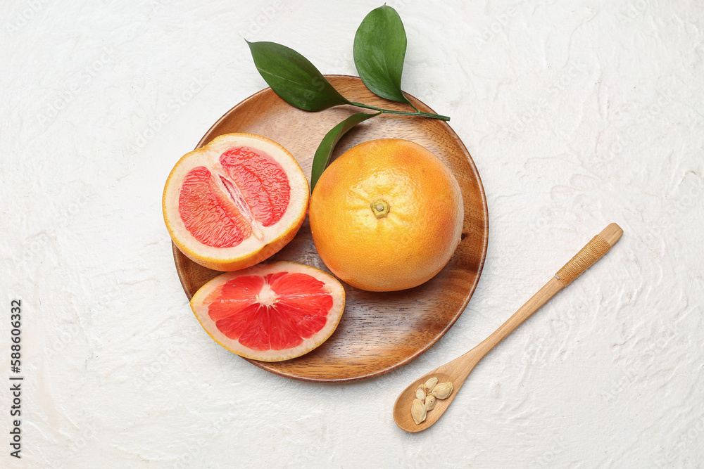 Wooden plate with ripe grapefruits and seeds on light background