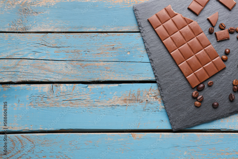 Slate board with tasty chocolate and coffee beans on color wooden background