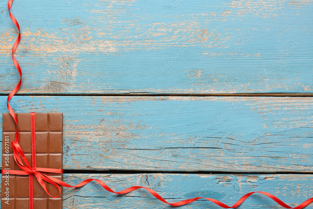 Tasty chocolate bar tied with red ribbon on color wooden background