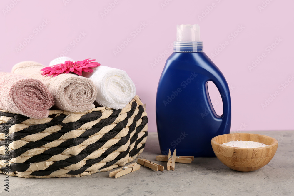 Laundry detergents, clothespins and basket with rolled towels on table against pink background