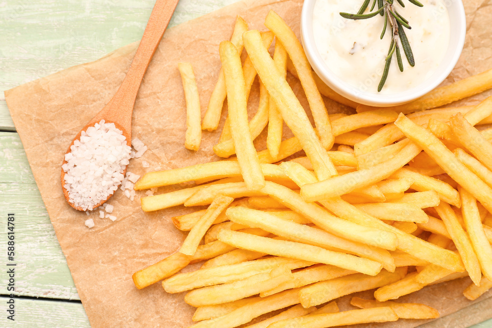 Tasty french fries, mayonnaise and salt on green wooden background