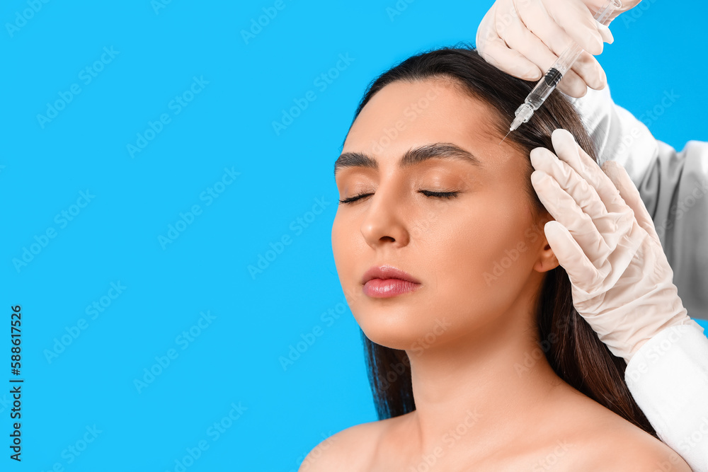 Young woman receiving filler injection in face against blue background