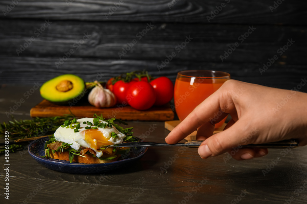 Woman cutting tasty egg Benedict at table