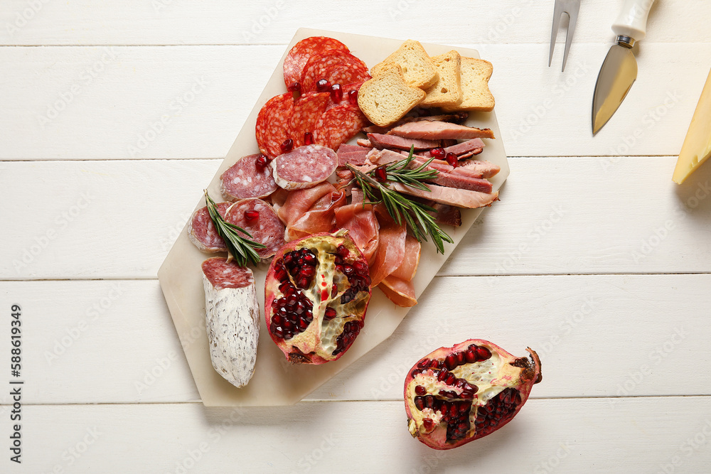 Board with assortment of tasty deli meats on white wooden background