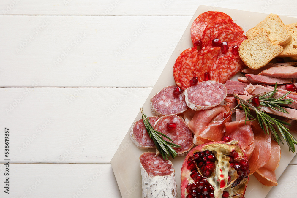 Board with assortment of tasty deli meats on white wooden background, closeup