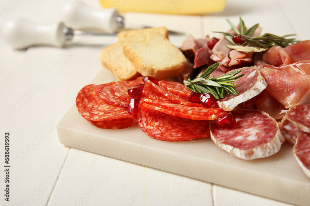 Board with assortment of tasty deli meats on white wooden background, closeup