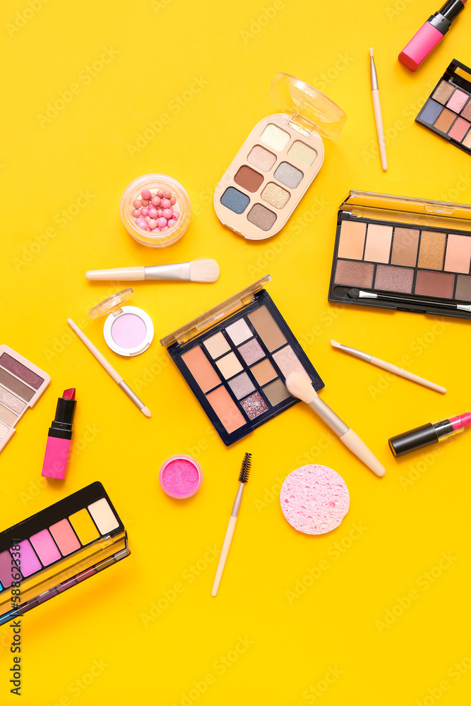 Decorative cosmetics with makeup brushes on yellow background