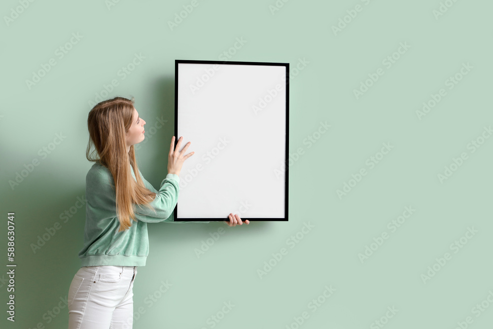 Young woman hanging blank frame on green wall