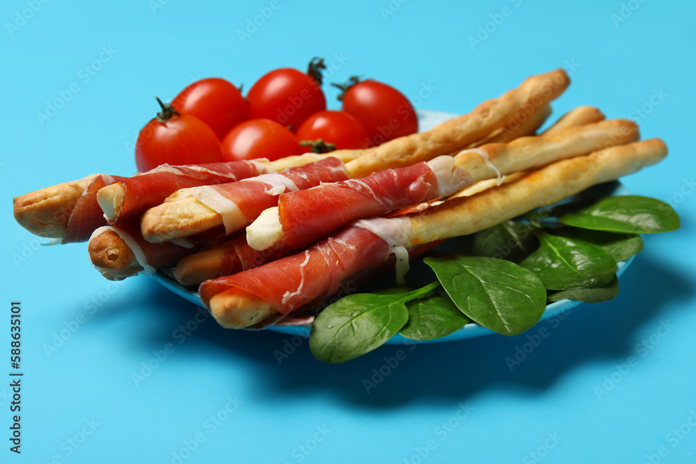 Plate of tasty Italian Grissini with bacon on blue background