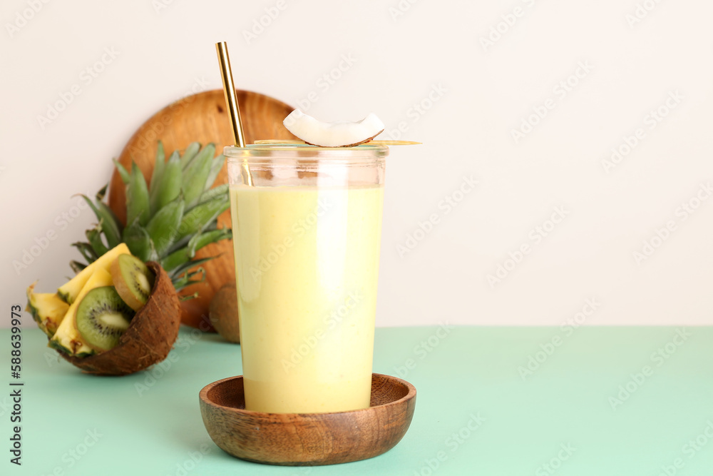 Glass of tasty pineapple smoothie, kiwi and coconut on color background