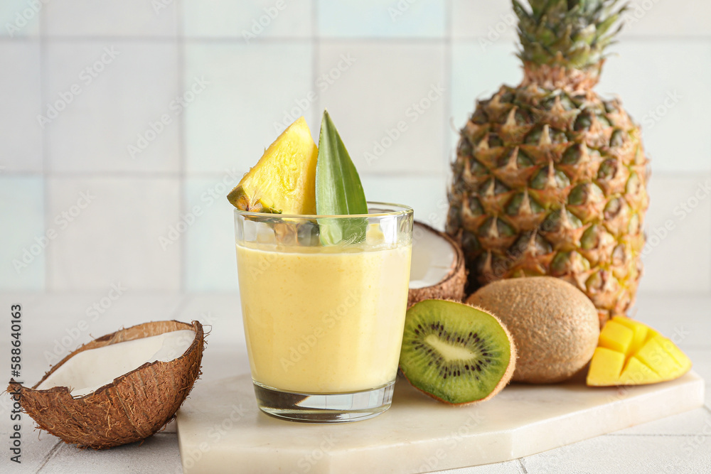 Glass of tasty pineapple smoothie, kiwi and coconut on tile table