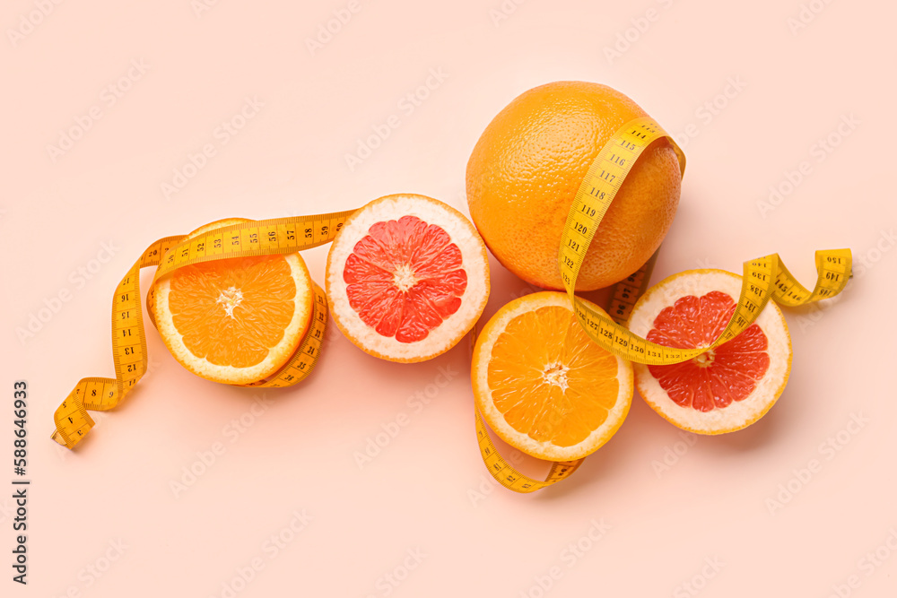 Cut oranges and yellow measuring tape on pink background. Diet concept