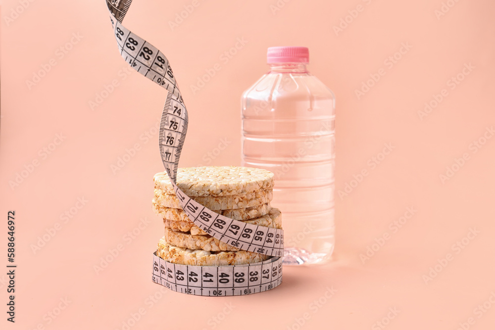 Rice cakes, bottle of water and measuring tape on pink background. Diet concept