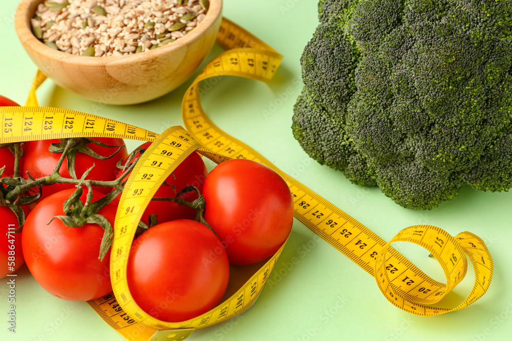 Fresh vegetables, bowl of seeds and yellow measuring tape on green background. Diet concept