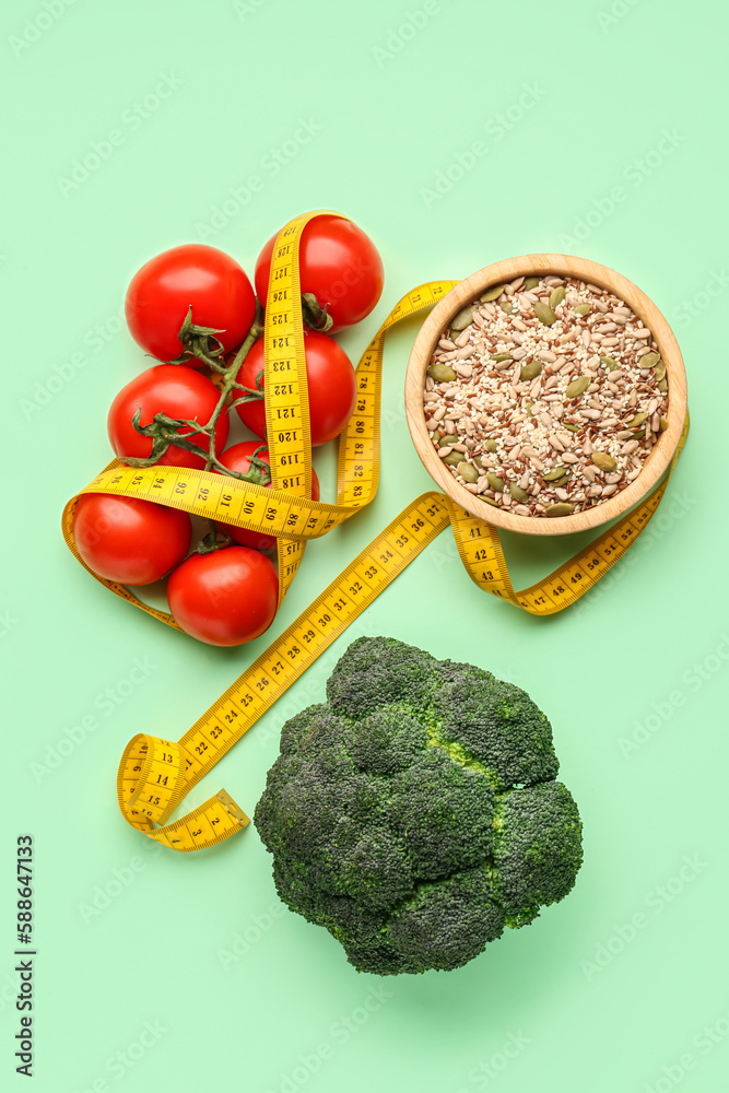 Fresh vegetables, bowl of seeds and yellow measuring tape on green background. Diet concept