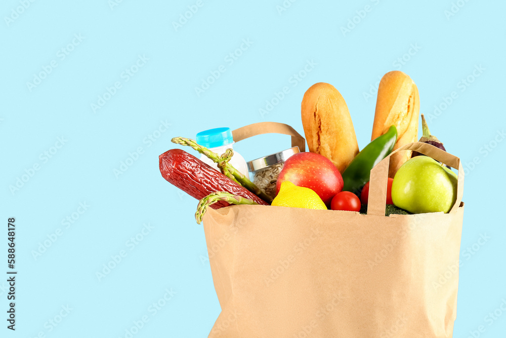 Paper bag with vegetables, fruits, sausage, bread and milk on light blue background