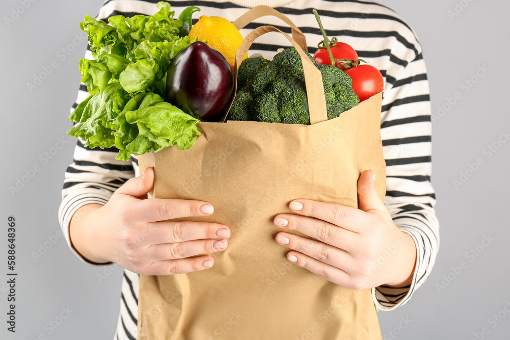 Woman holding paper bag with vegetables and fruits on grey background