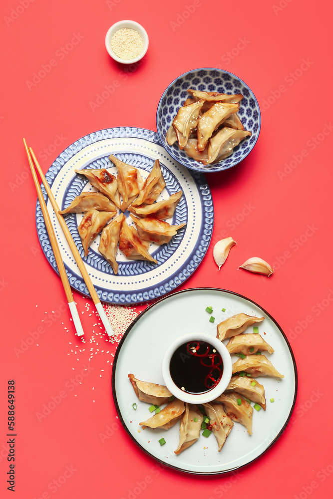 Plates with tasty Chinese jiaozi and sauce on red background