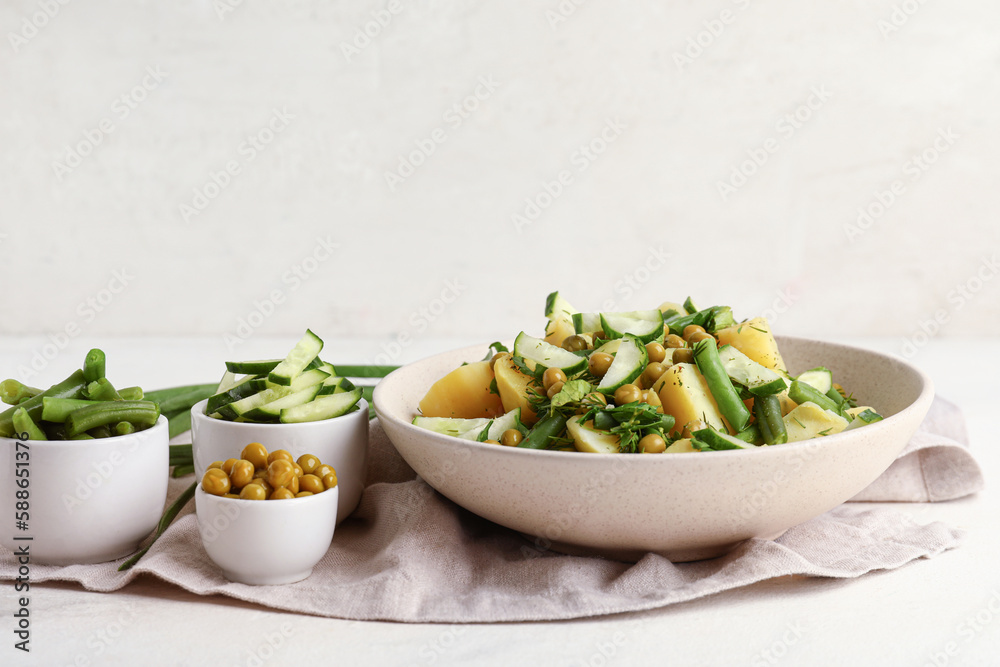 Bowl of tasty Potato Salad with vegetables and ingredients on light background