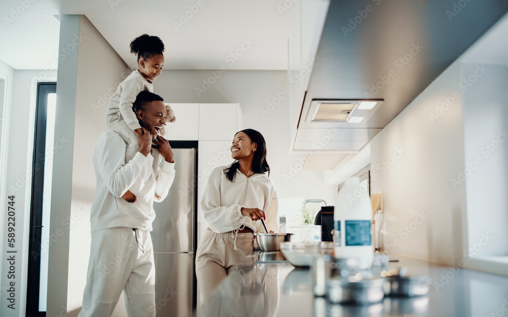 Black family showing parenthood, together in the kitchen - dad carrying daughter, mom cooking