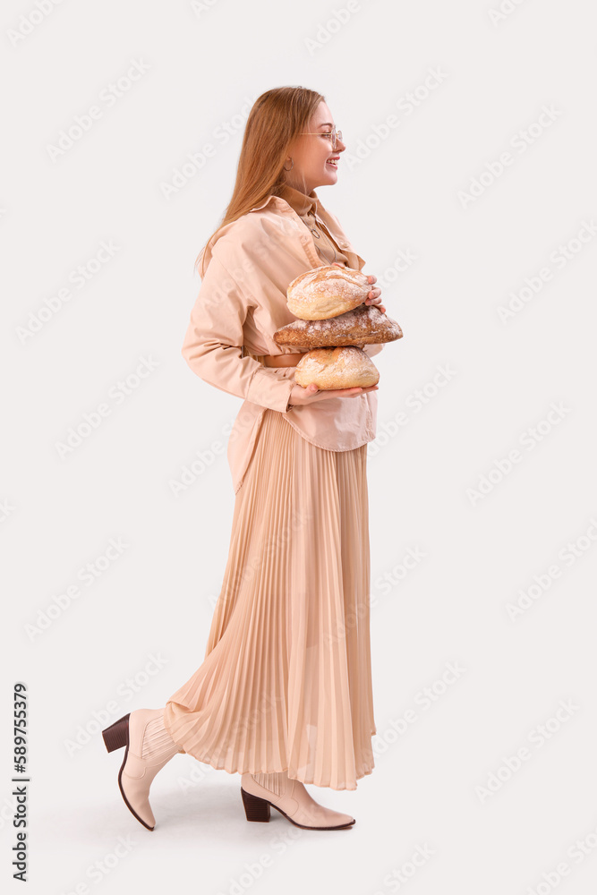 Young woman with loaves of fresh bread on light background