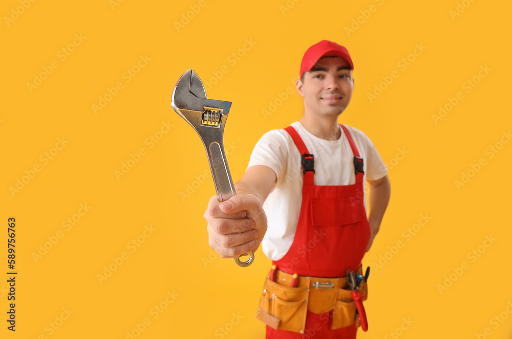 Young plumber with wrench on yellow background