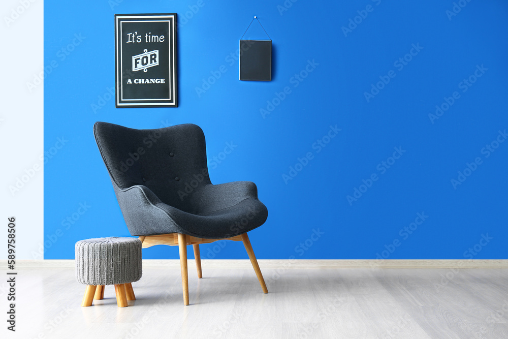 Stylish grey armchair, pouf and poster with text ITS TIME FOR A CHANGE near blue wall