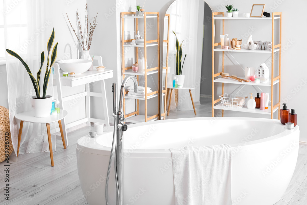 Interior of bathroom with bathtub, mirror and shelving units