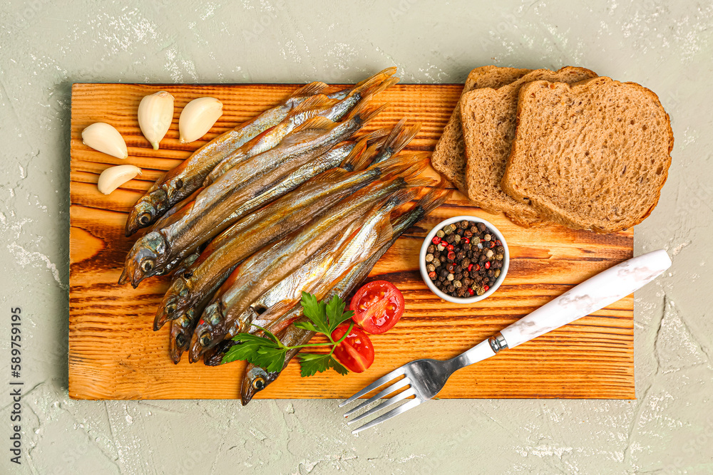 Board with tasty smoked capelin and bread pieces on grey background