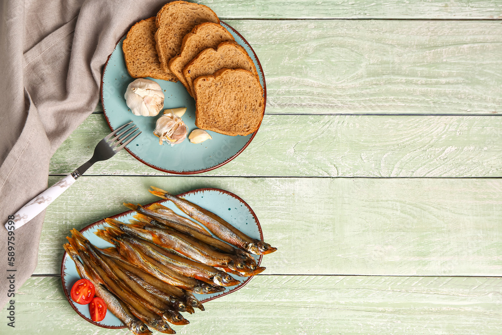 Plate tasty smoked capelin, bread pieces and garlic on green wooden background