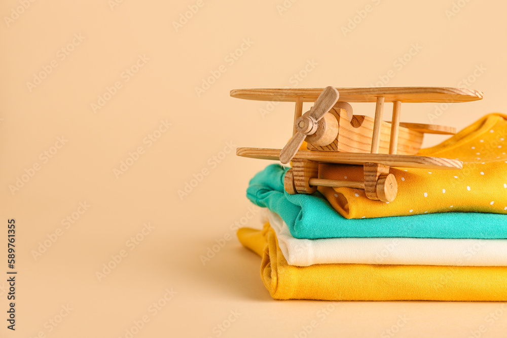 Stack of baby clothes and wooden toy plane on color background