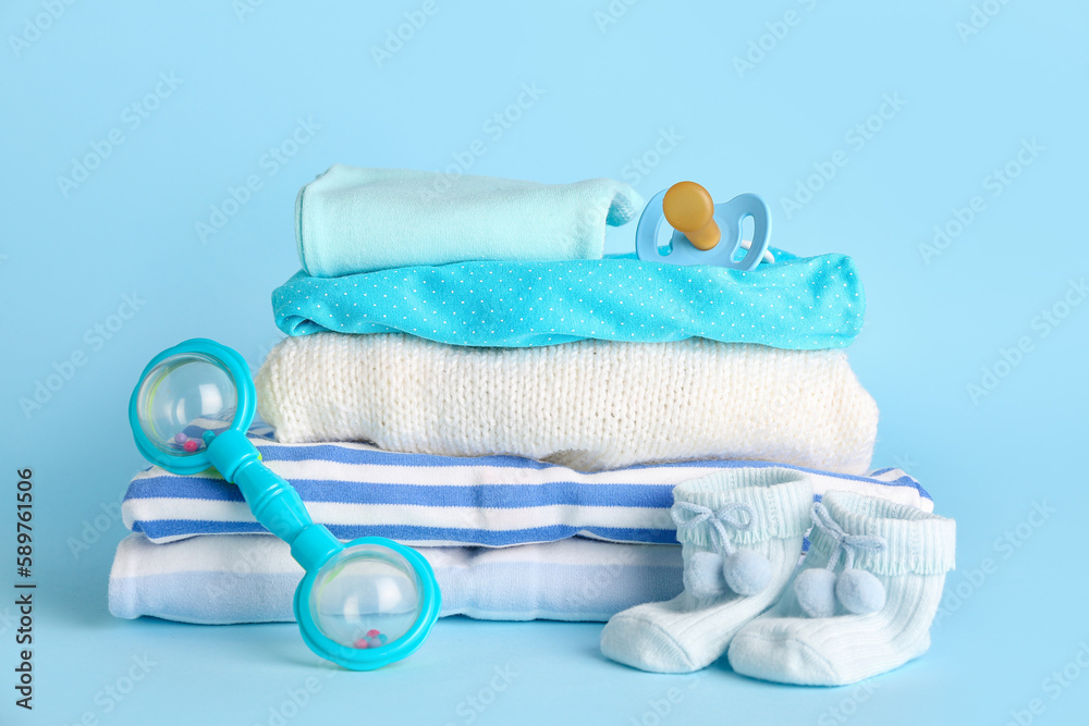 Stack of baby clothes, rattle and pacifier on color background