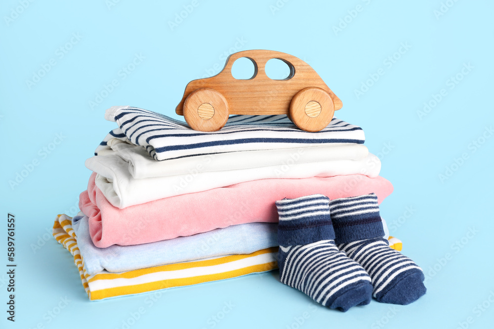 Stack of baby clothes, socks and wooden toy on color background