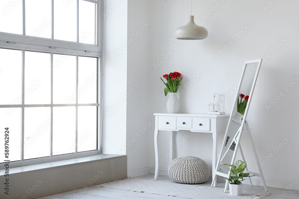 Interior of light room with mirror and tulips in vase on table