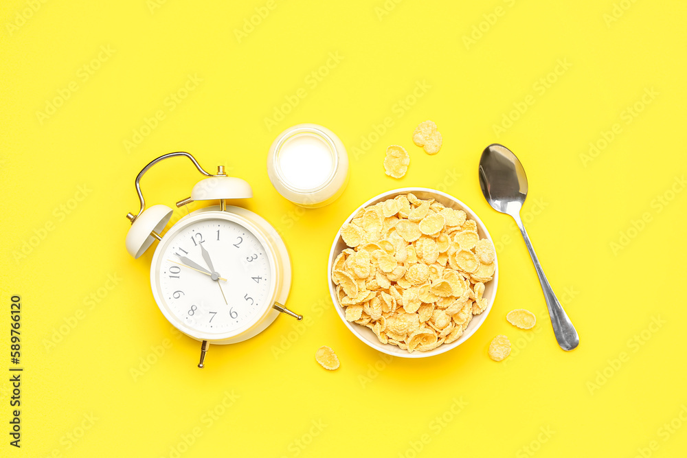 Composition with alarm clock, bowl of corn flakes and milk on yellow background