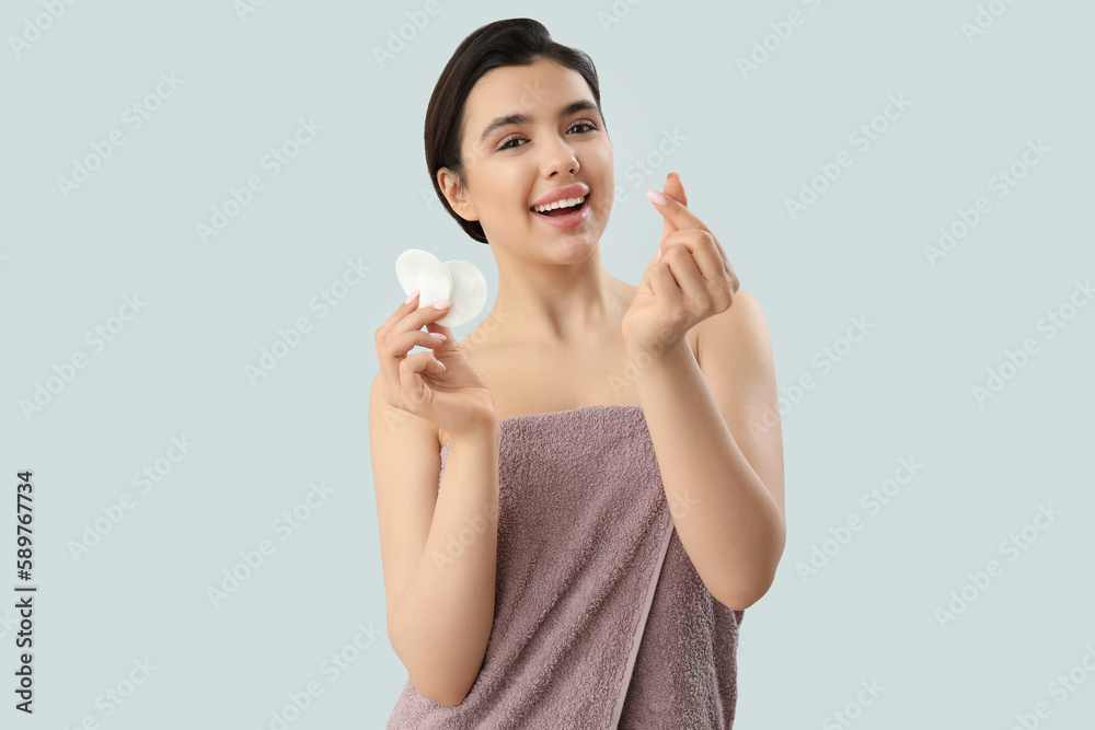 Young woman with cotton pads making heart on light background