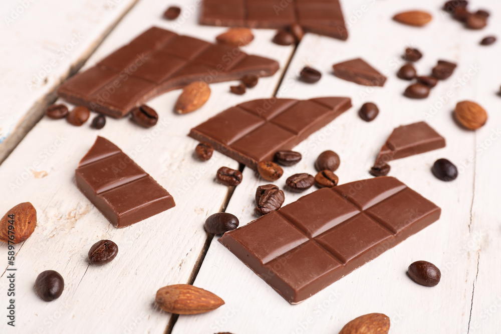 Pieces of tasty chocolate, almonds and coffee beans on light wooden background, closeup