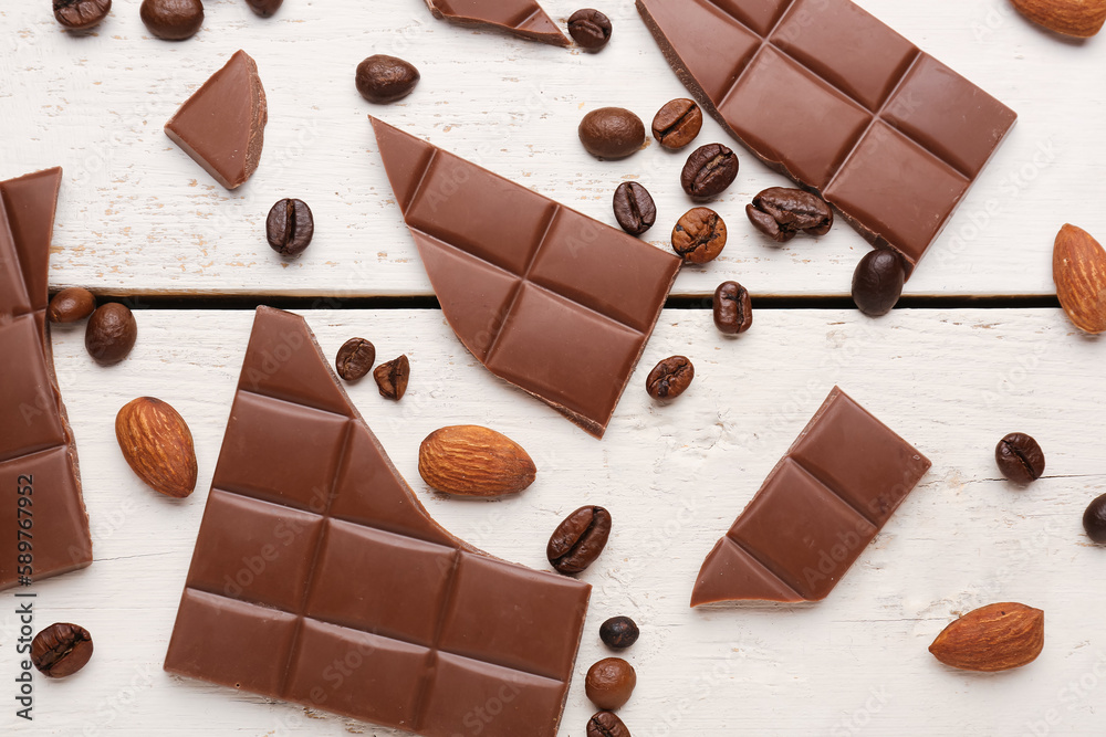 Composition with pieces of tasty chocolate, almonds and coffee beans on light wooden background