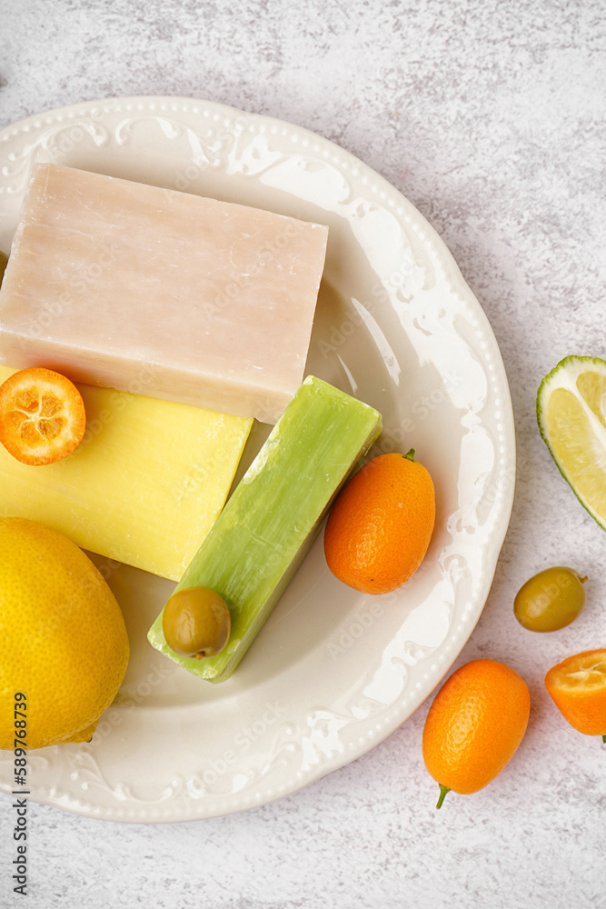 Plate with natural soap bars, citrus fruits and olives on light background, closeup