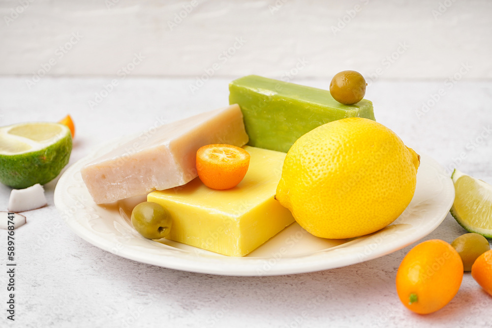 Plate with natural soap bars, citrus fruits and olives on light background, closeup