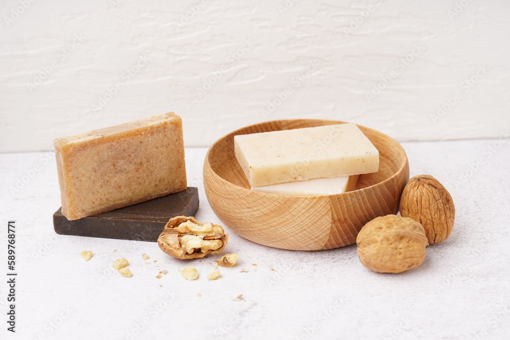 Bowl with natural soap bars and walnuts on light background