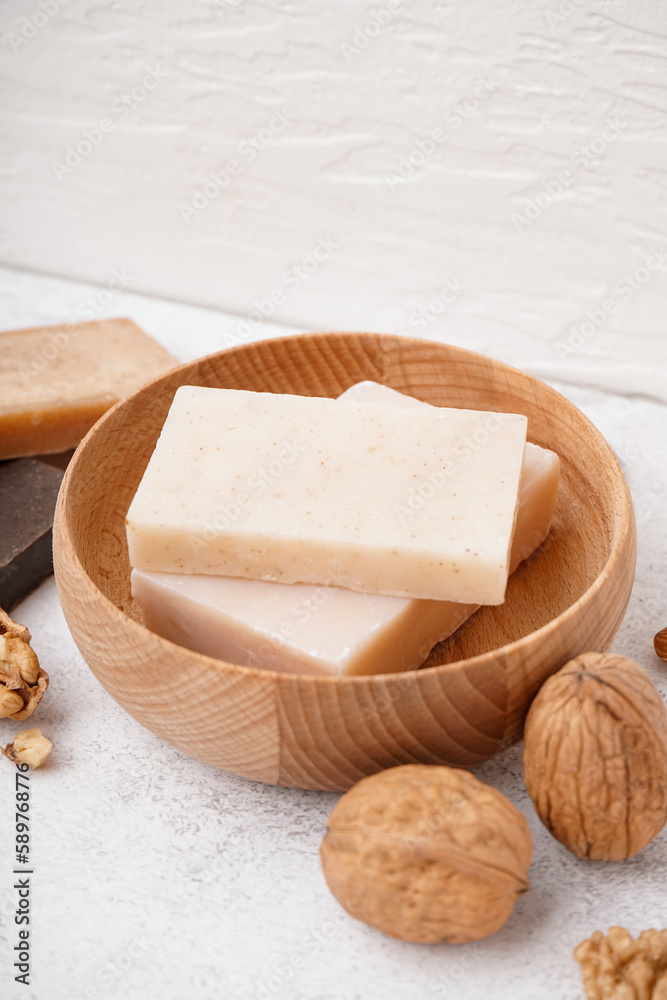 Bowl with natural soap bars and walnuts on light background, closeup