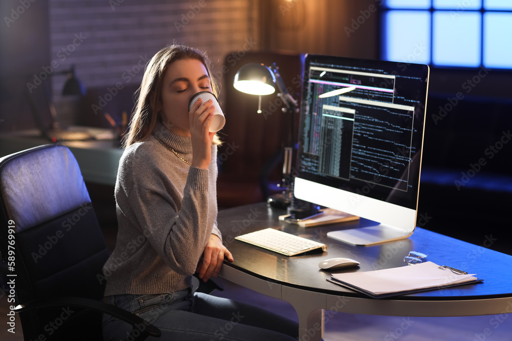 Female programmer drinking coffee in office at night