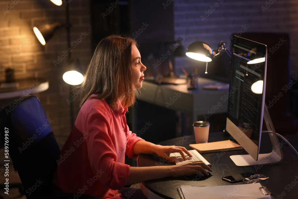 Female programmer working with computer in office at night